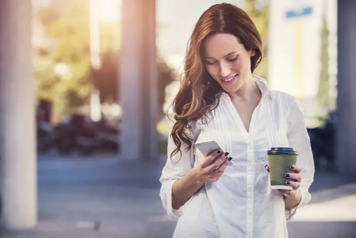 a woman is holding coffee and looking at her mobile phone