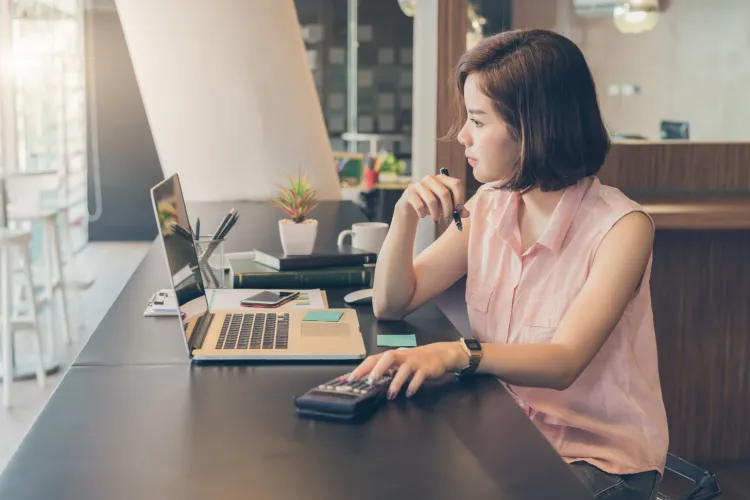 Woman using calculator and laptop at cafe counter