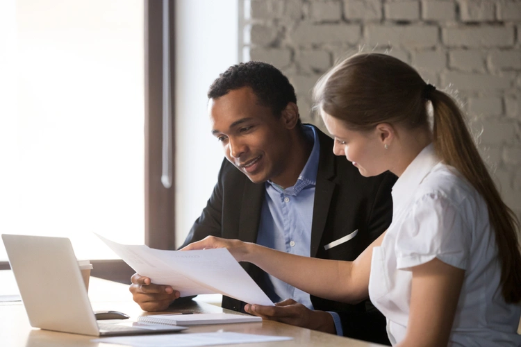 Two people reviewing paperwork beside a laptop