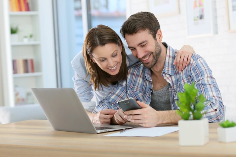 Couple looking at a phone beside a laptop and paperwork at home