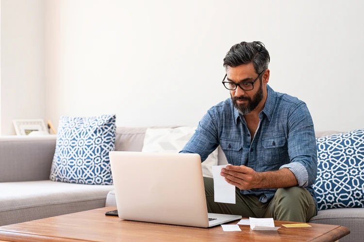 Man reviewing paperwork beside a laptop
