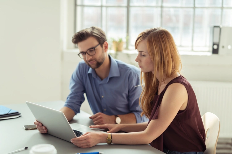 Two people reviewing paperwork beside a laptop