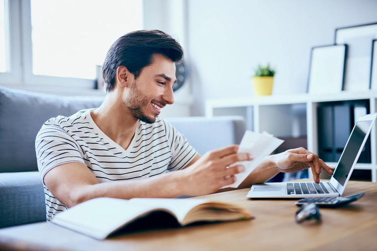 Man reviewing paperwork with a laptop and calculator at home