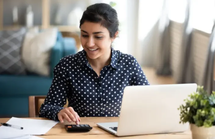 Smiling woman using calculator and laptop at home