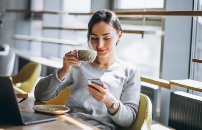 Woman sipping coffee while checking her phone